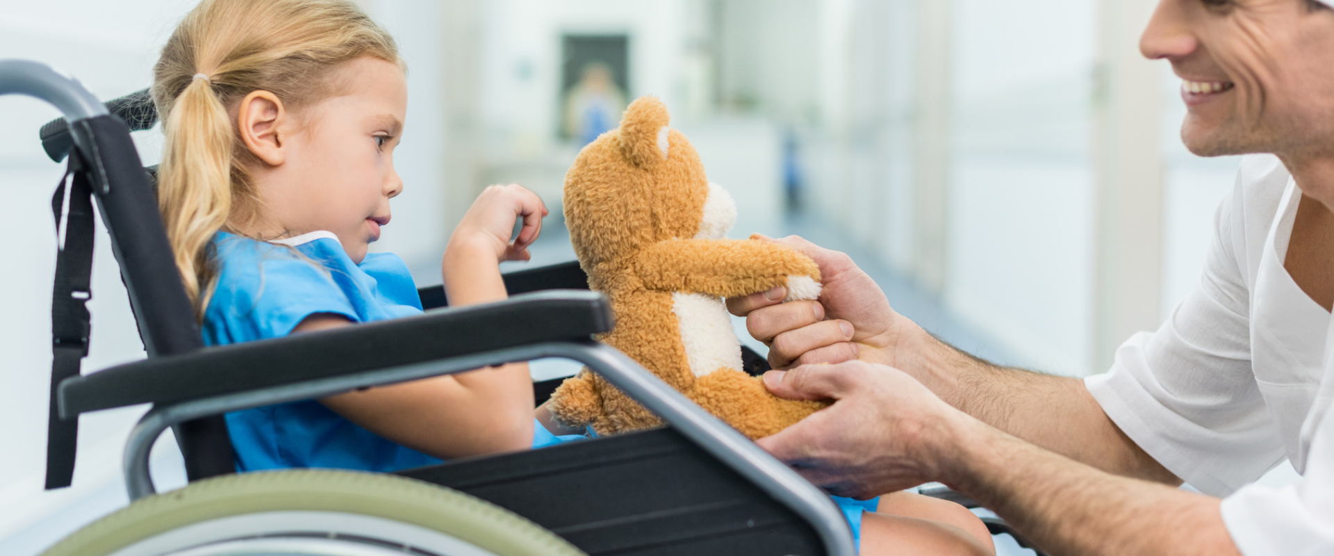 médico segurando um ursinho de pelúcia enquanto brinca com sua paciente criança que está na cadeira de rodas